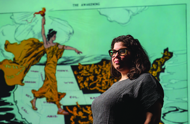 Monica Mercado, Assistant Professor of History, stands with a projection of The Awakening, an image of Lady Liberty about women’s suffrage by Henry Mayer, November 6, 2020.