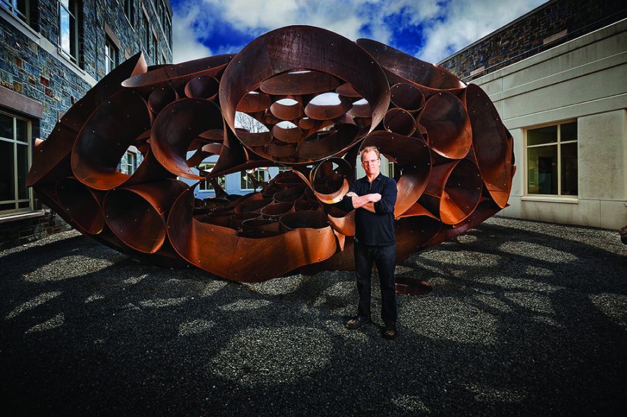 DeWitt Godfrey, Colgate University Professor of Art, and Chair of the Art and Art History Department, poses with his sculpture, Odin, in the courtyard of the Ho Science Center.